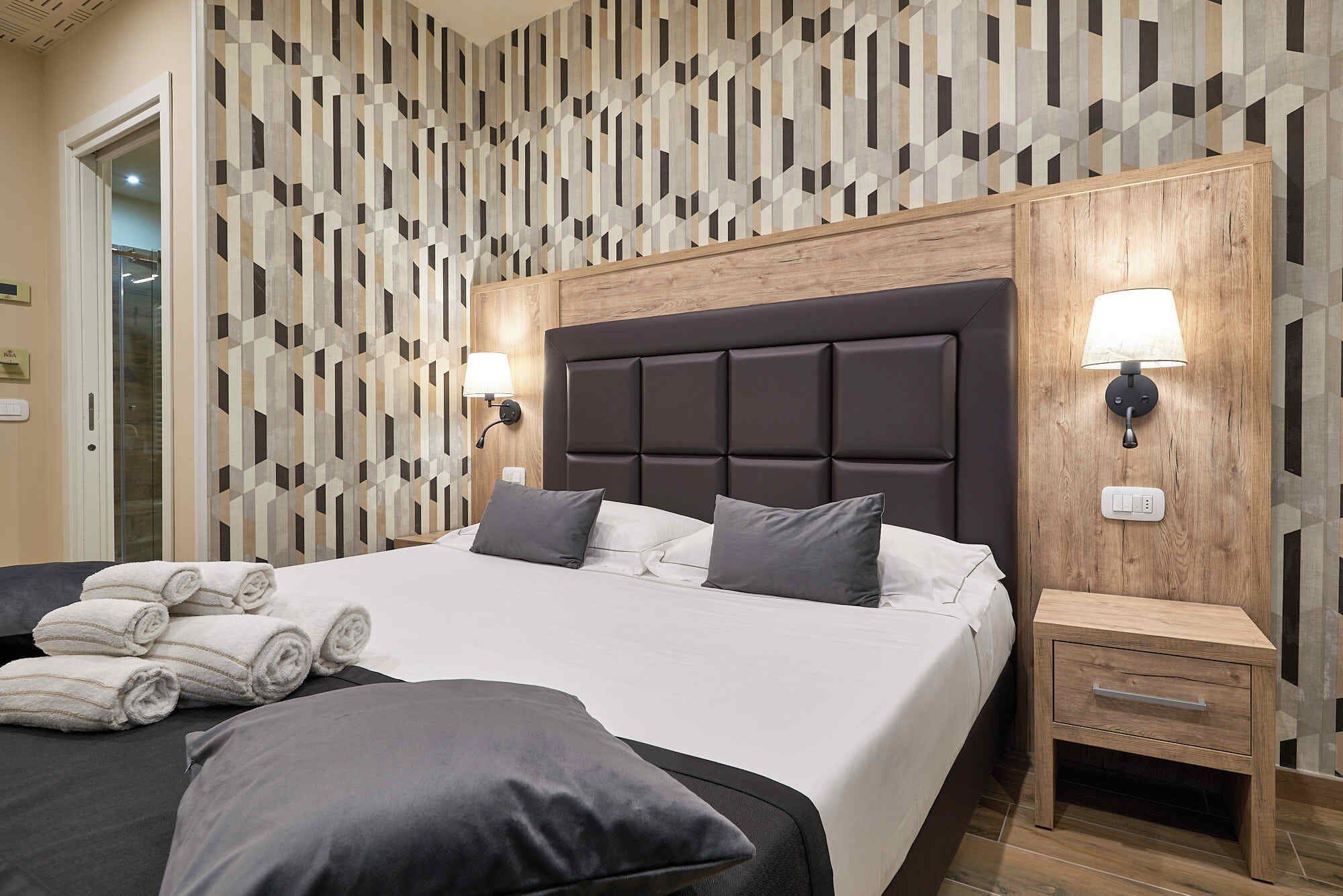 Ein modernes Hotelzimmer mit einem großen Bett, zwei Nachttischen und einer Wand mit geometrischem Muster.