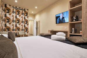 Habitación de hotel con una cama, un televisor fijado a la pared, un estante de madera con una tetera y un papel tapiz estampado.