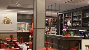 A restaurant with tables and chairs, a bar area with shelves of bottles, and a logo on the wall.