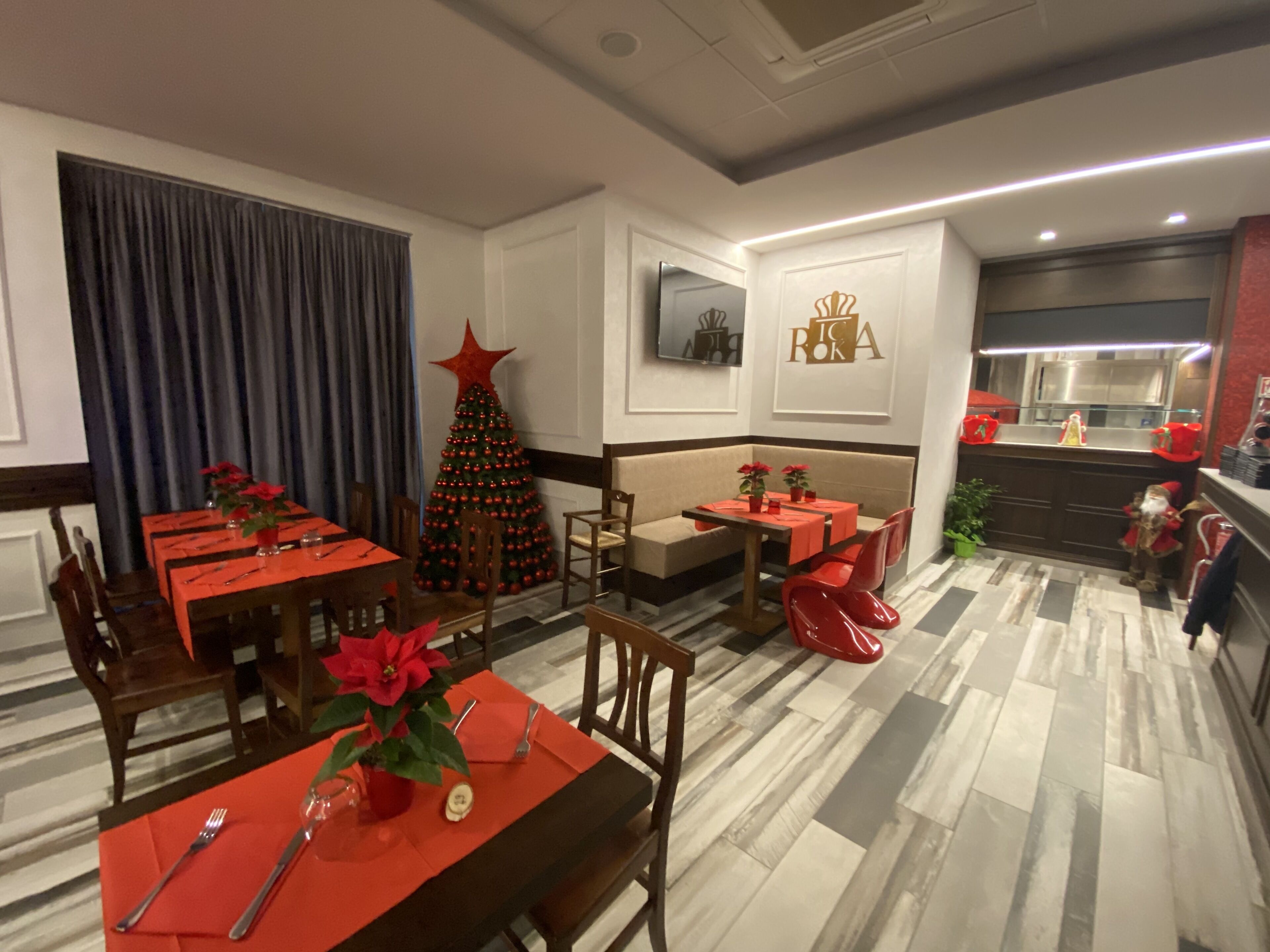 A dining area with red tables and chairs, a Christmas tree, and a kitchen area with red accents.