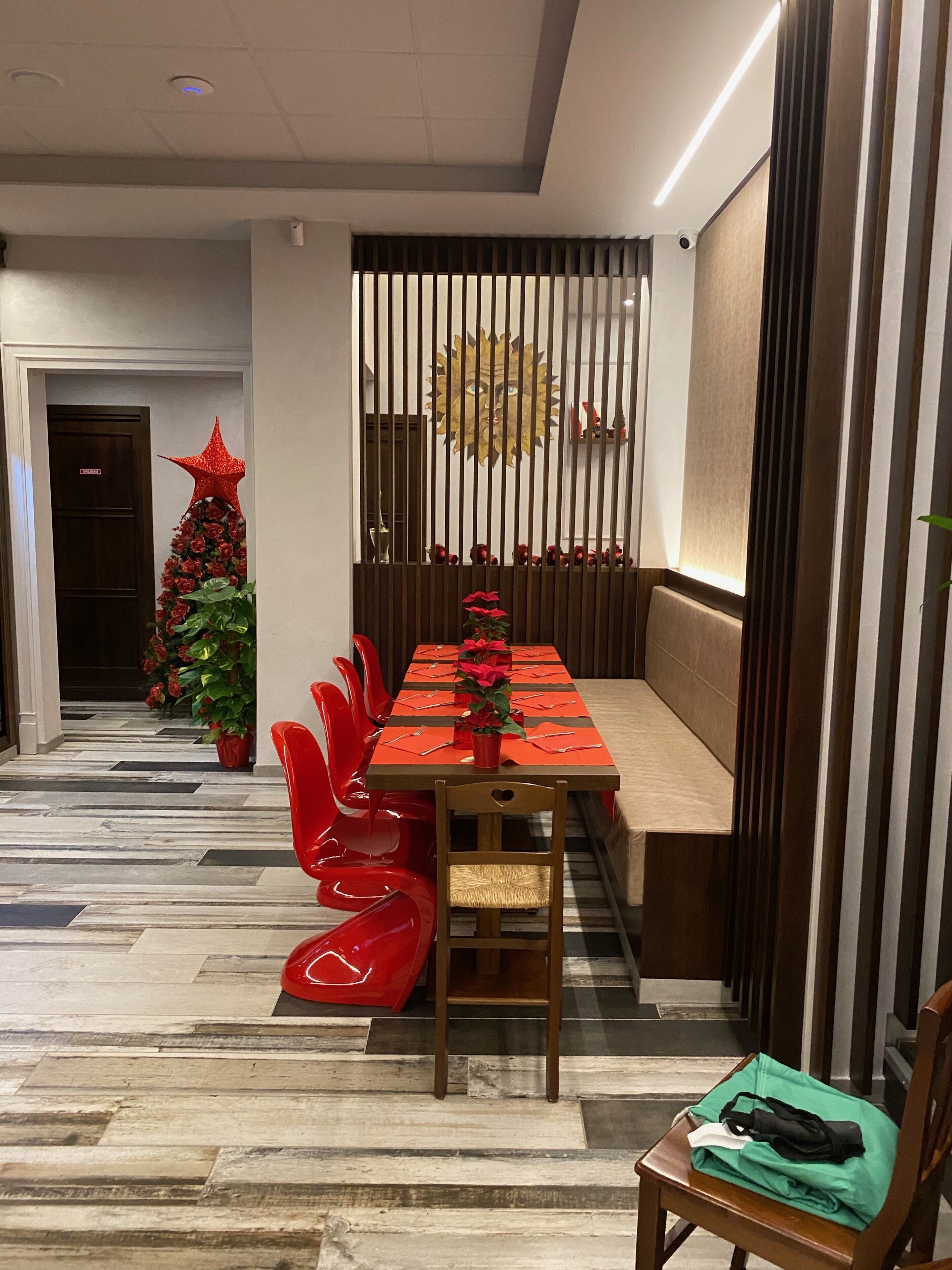 Een eetgedeelte met een lange tafel gedekt voor meerdere personen, een kerstboom en rode stoelen.