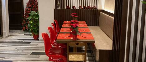 A dining area with a long table set for multiple people, a Christmas tree, and red chairs.