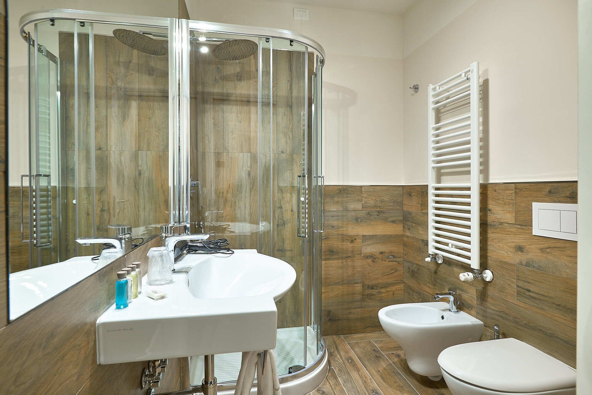 A modern bathroom with a glass shower enclosure, a white sink, a bidet, and a toilet.