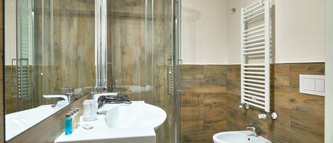 A modern bathroom with a glass shower enclosure, a white sink, a bidet, and a toilet.