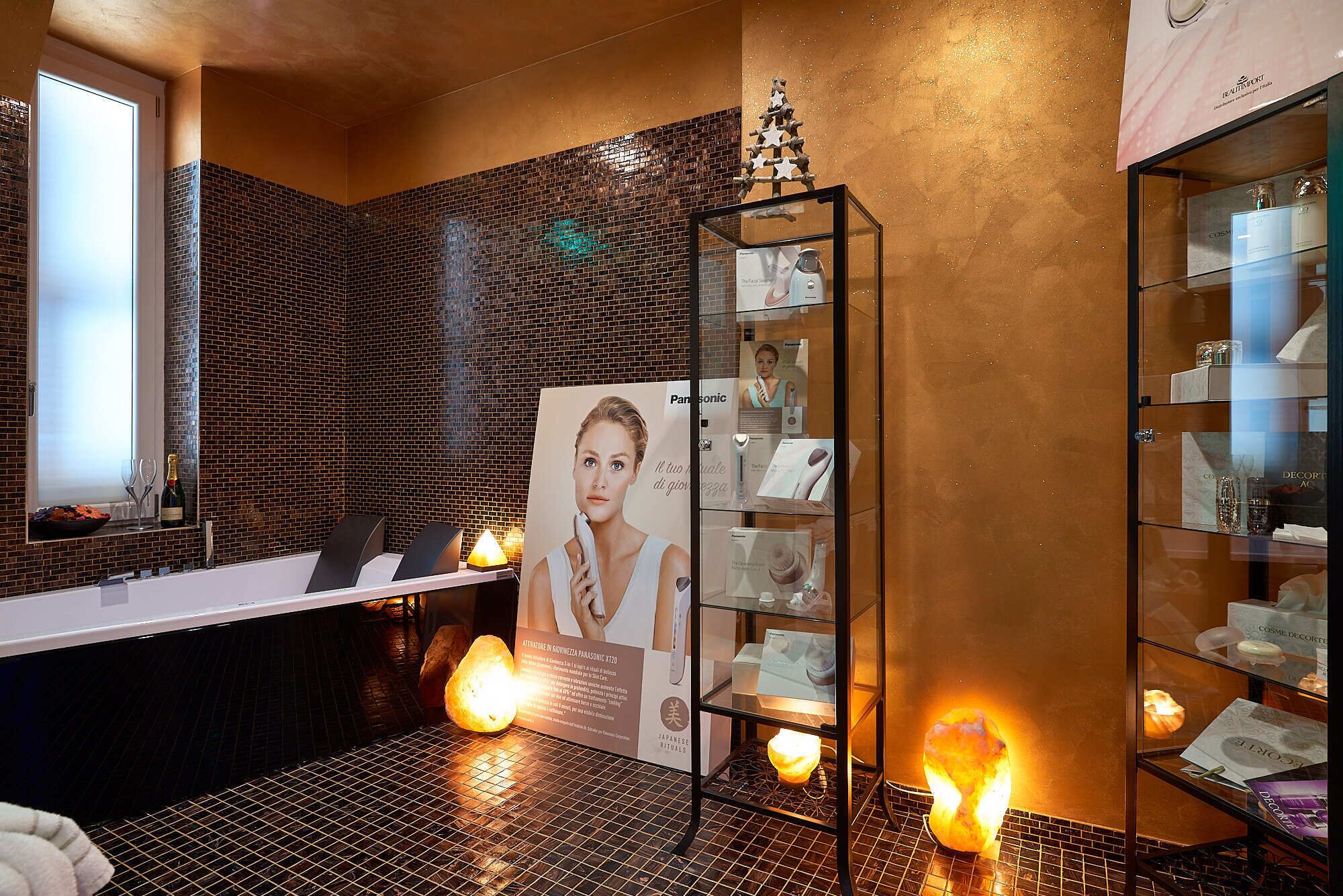 Une salle de bain avec un mur carrelé, une vitrine en verre contenant des produits et un arbre décoratif.