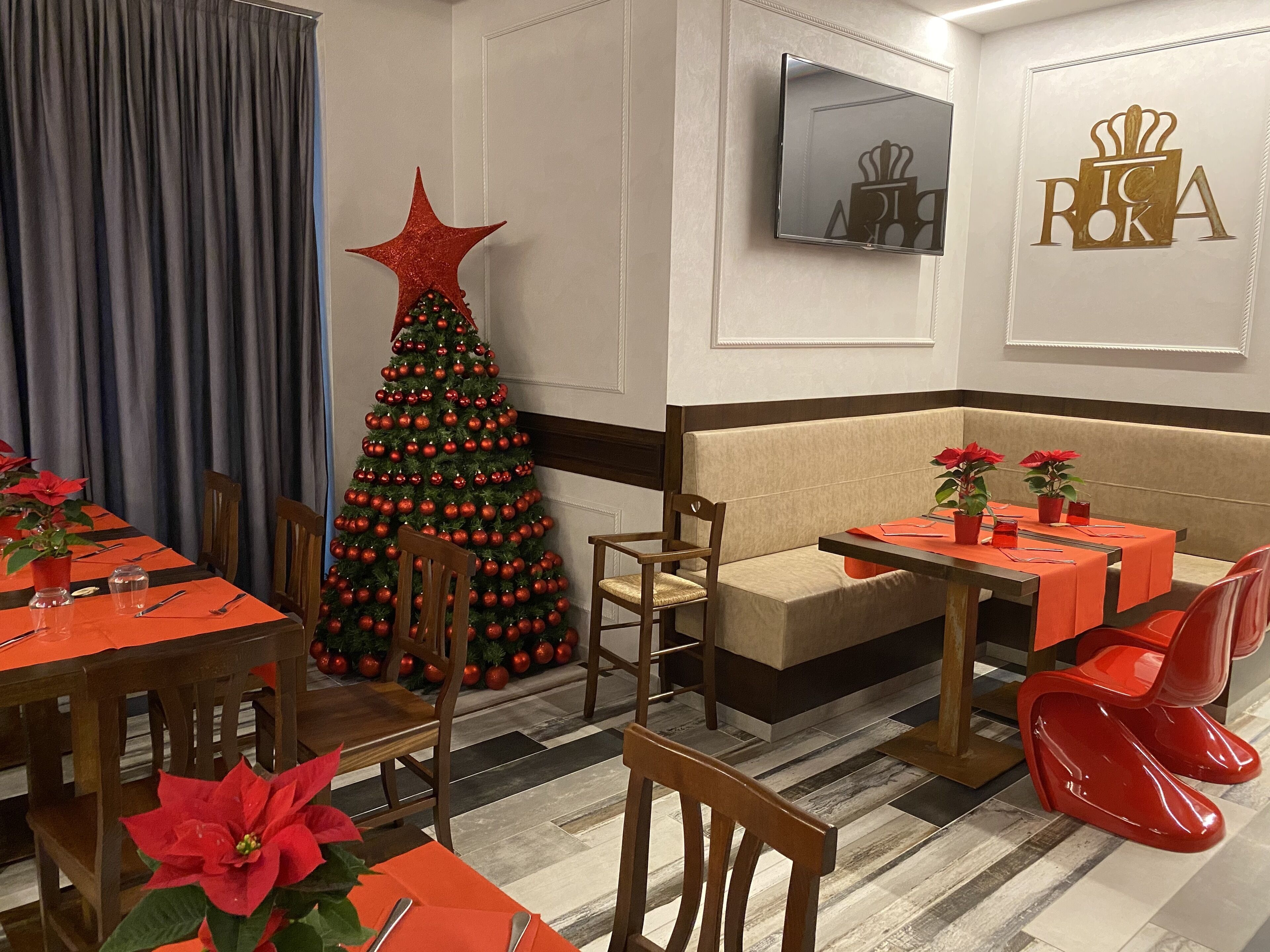 Un espace de restauration d’hôtel décoré d’un sapin de Noël, avec des chaises rouges et des tables mises pour le repas.