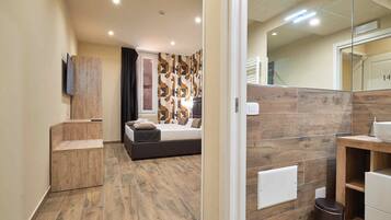 A modern bedroom with a wooden floor, a bed with pillows, a bedside table, and a mirror.