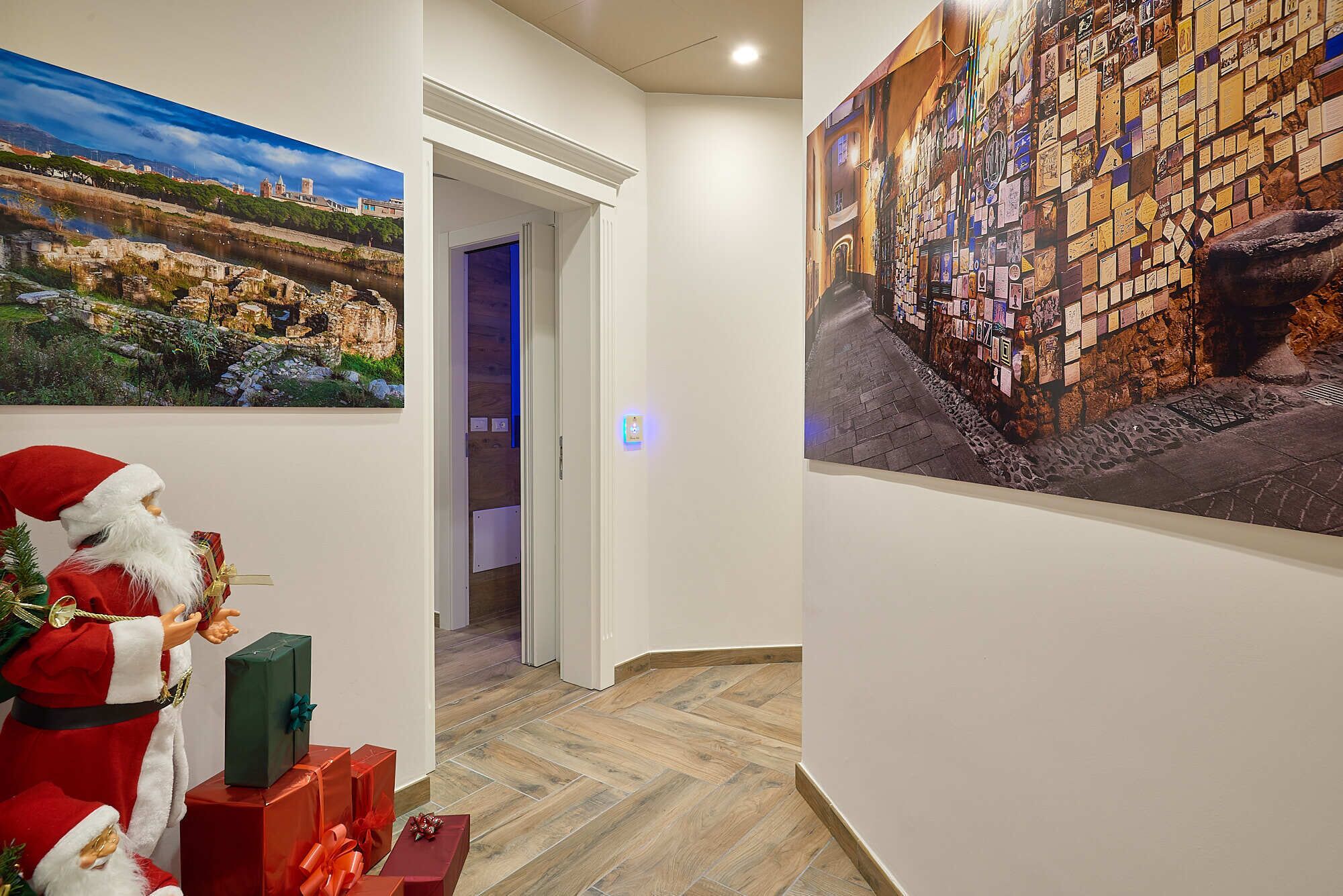 A hallway with a Christmas decoration, a painting of a historical building, and a wall covered with postcards.