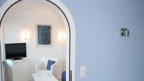 Una habitación con televisión, una silla blanca, una mesita y un cuadro en la pared.