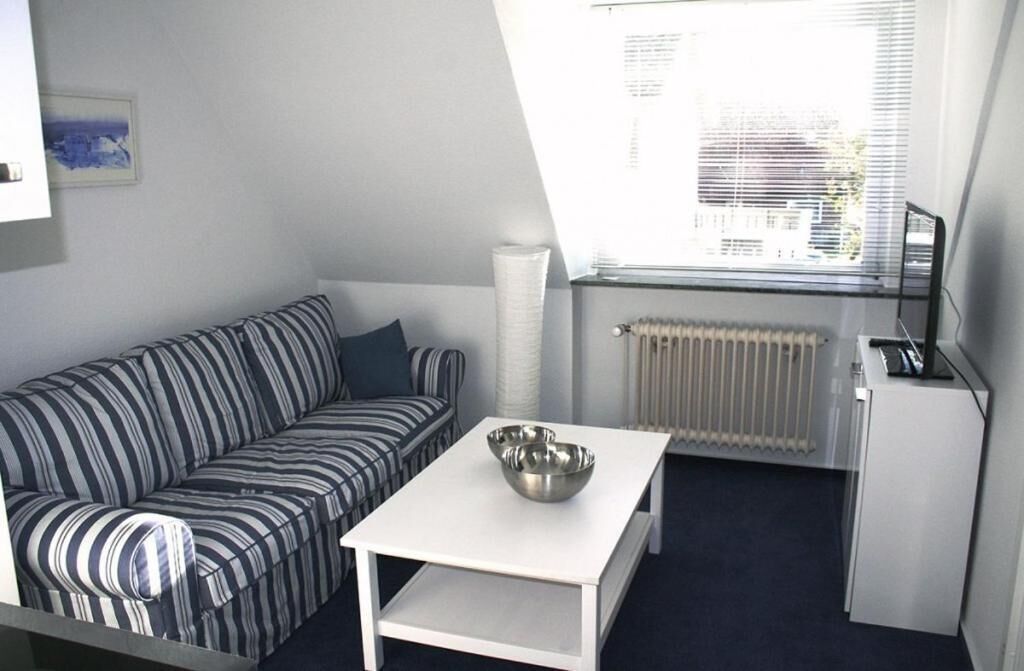 A small, modern room with a striped sofa, a white table with a metal bowl, a radiator, and a window with blinds.