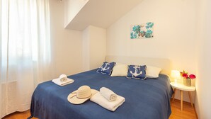 A bedroom with a bed, pillows, a nightstand, a lamp, and a painting on the wall. - Apartments Mondo (Dubrovnik)