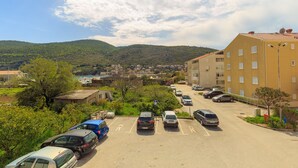 A parking lot with several cars, a building with multiple windows, and a mountainous landscape in the background. - Apartments Mondo (Dubrovnik)