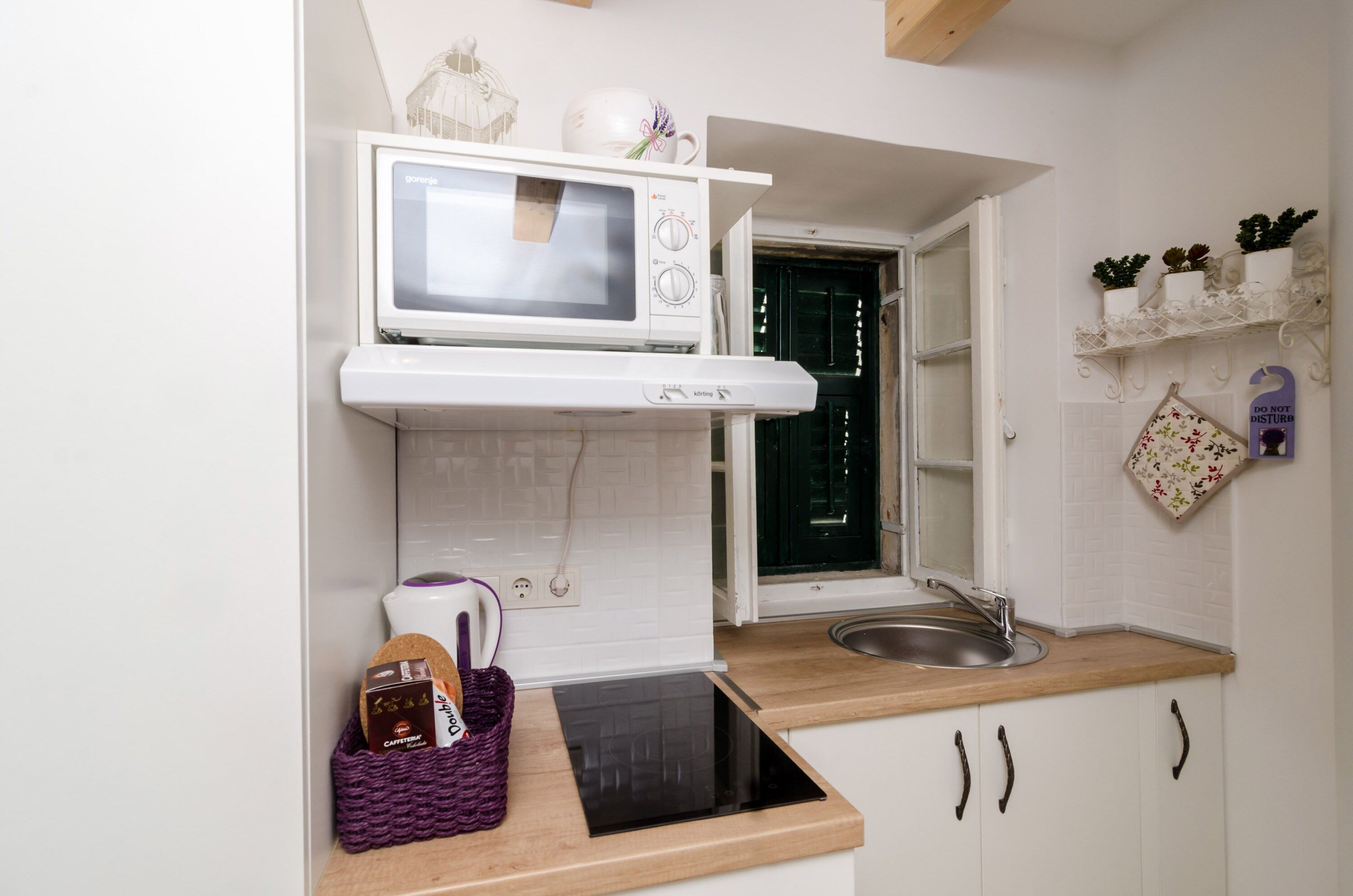 A compact kitchen with a microwave, a built-in oven, a sink, and a small window.