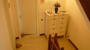 A staircase with a wooden handrail leading to a landing. A white dresser with drawers and a vase of flowers is on the landing. - Dimora di Bosco Room & Breakfast (Rubano)
