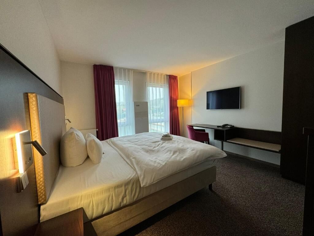 Une chambre d’hôtel avec un lit, un bureau, une télévision et une fenêtre avec des rideaux.