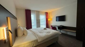 Une chambre d’hôtel avec un lit, un bureau, une télévision et une fenêtre avec des rideaux.
