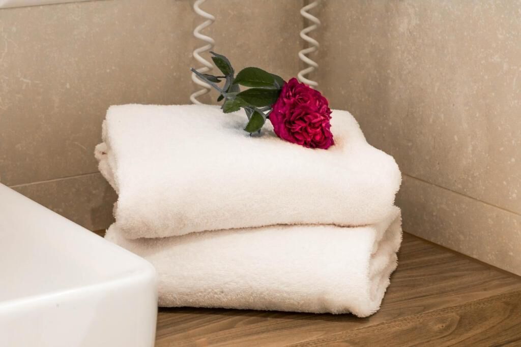 A stack of white towels on a wooden surface with a red flower on top.