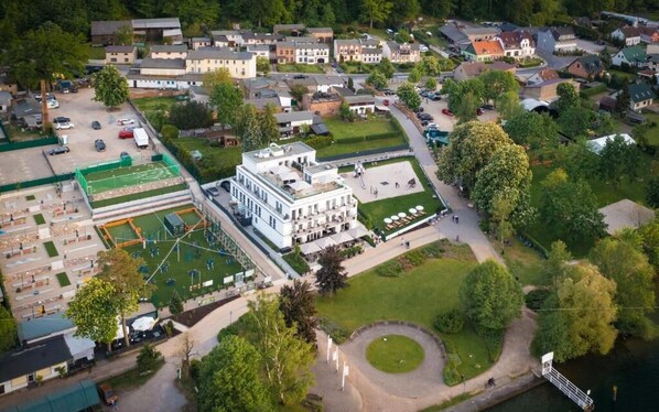 Vista aérea de una zona residencial con un edificio blanco destacado, un campo deportivo verde y una masa de agua.