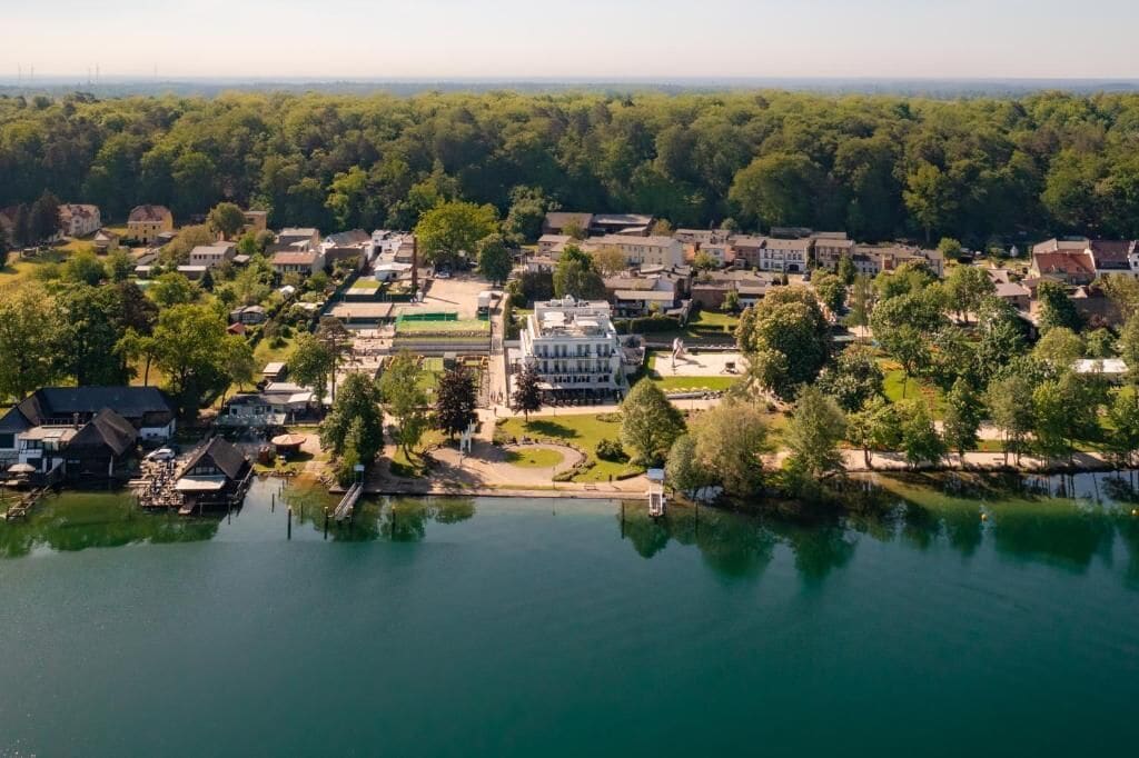 An aerial view of a lakeside town with residential buildings, a central park, and a large white building.