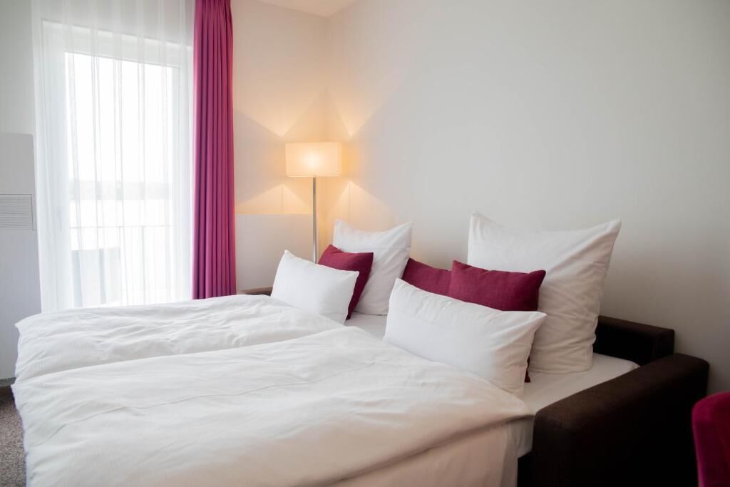 Une chambre d’hôtel avec un lit, des oreillers, une lampe et une fenêtre avec des rideaux.