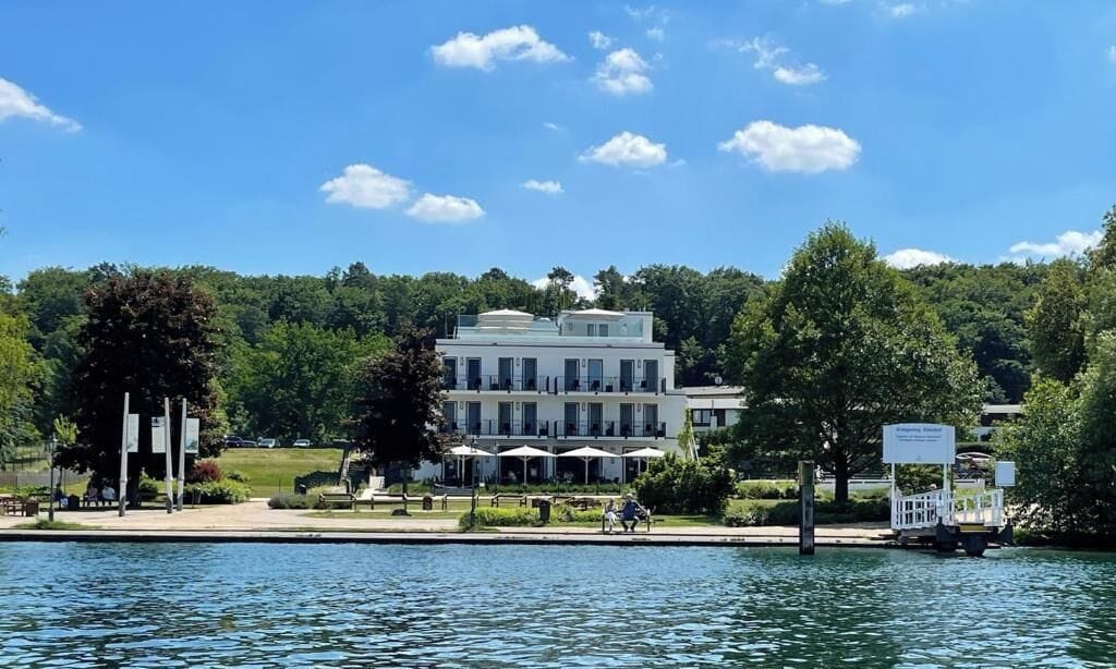 A lakeside hotel with a large building, outdoor seating, and a dock.