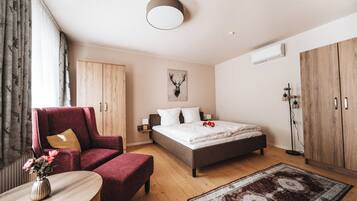 Een moderne slaapkamer met een bed, een rode fauteuil, een houten garderobe en een tafeltje met een vaas.