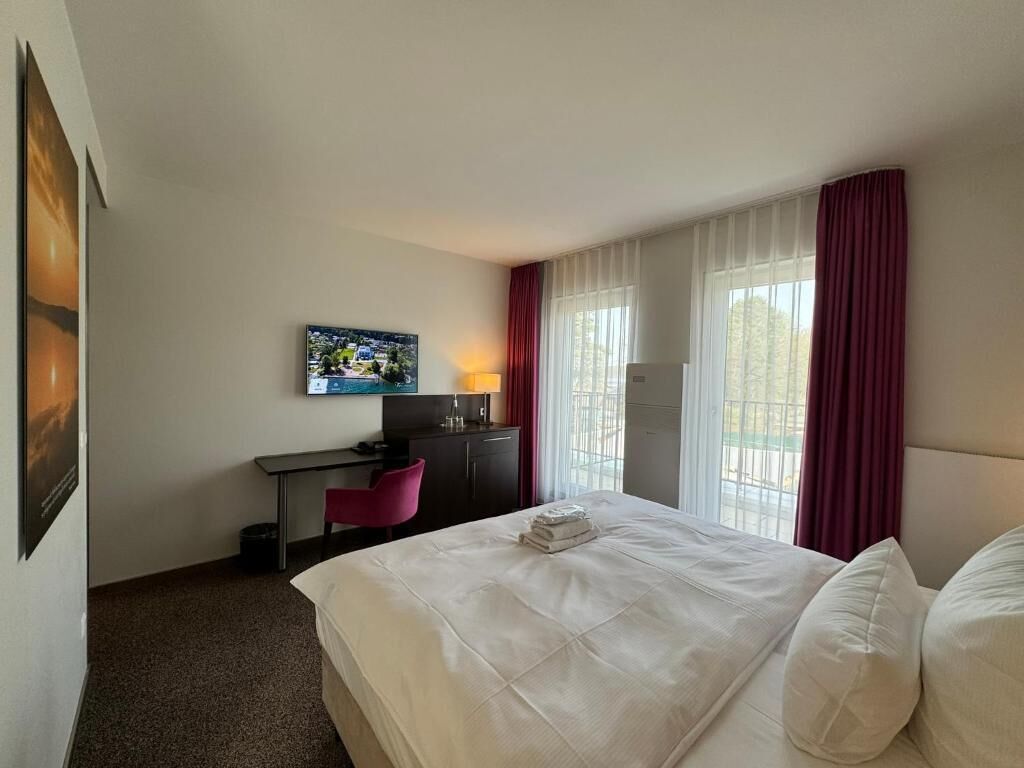 Een hotelkamer met een bed, bureau, stoel, televisie en een raam met gordijnen.