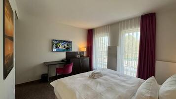 Een hotelkamer met een bed, bureau, stoel, televisie en een raam met gordijnen.
