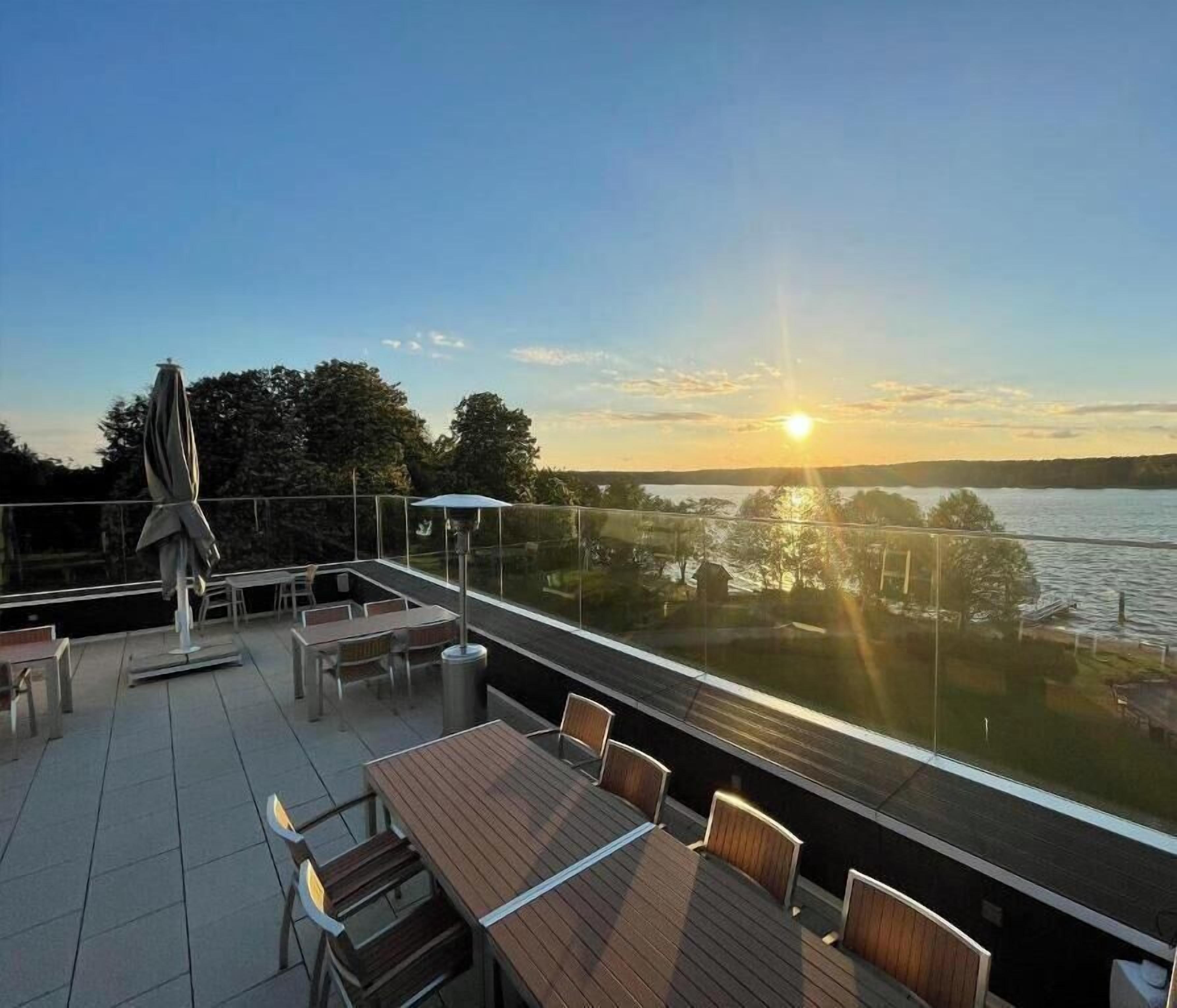 Terraço com mesas e cadeiras, com vista para a água e árvores.