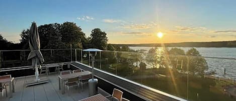 A terrace with tables and chairs, overlooking a body of water and trees.