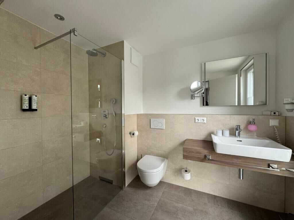 A modern bathroom with a glass-enclosed shower, a white toilet, and a wooden vanity with a sink.
