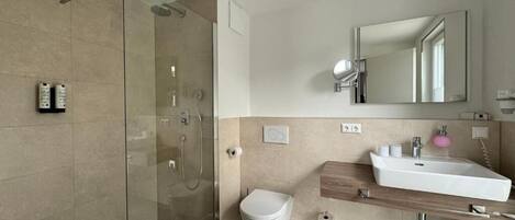 Un baño moderno con ducha envuelta en vidrio, inodoro blanco y tocador de madera con lavamanos.