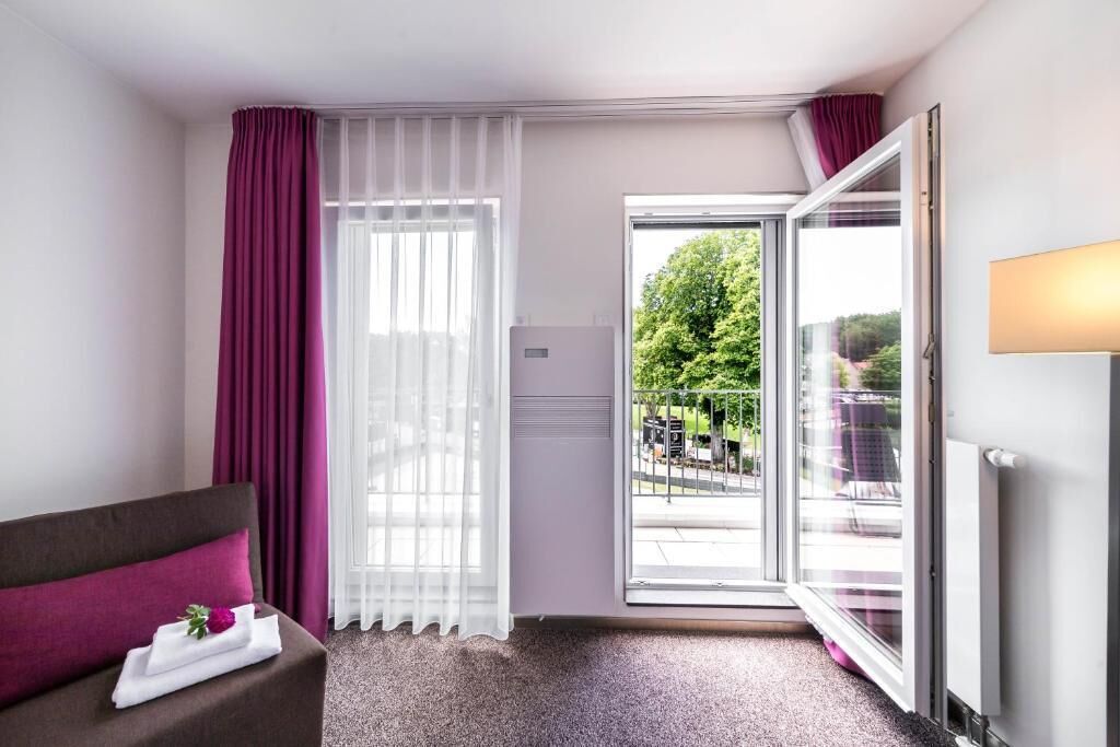 A hotel room with a bed, a window with curtains, a radiator, and a view of the outdoors.