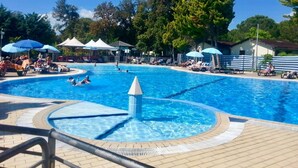 Ein Pool mit Liegestühlen und Sonnenschirmen, umgeben von Bäumen und blauem Himmel.