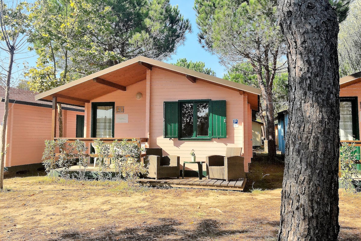 A row of small, single-story cabins with green shutters, a sign indicating '93', and a 'P' parking sign.