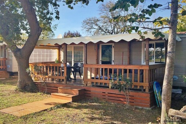 Una edificación de un solo nivel con una terraza de madera, un porche cubierto y un pequeño espacio de estar al aire libre.
