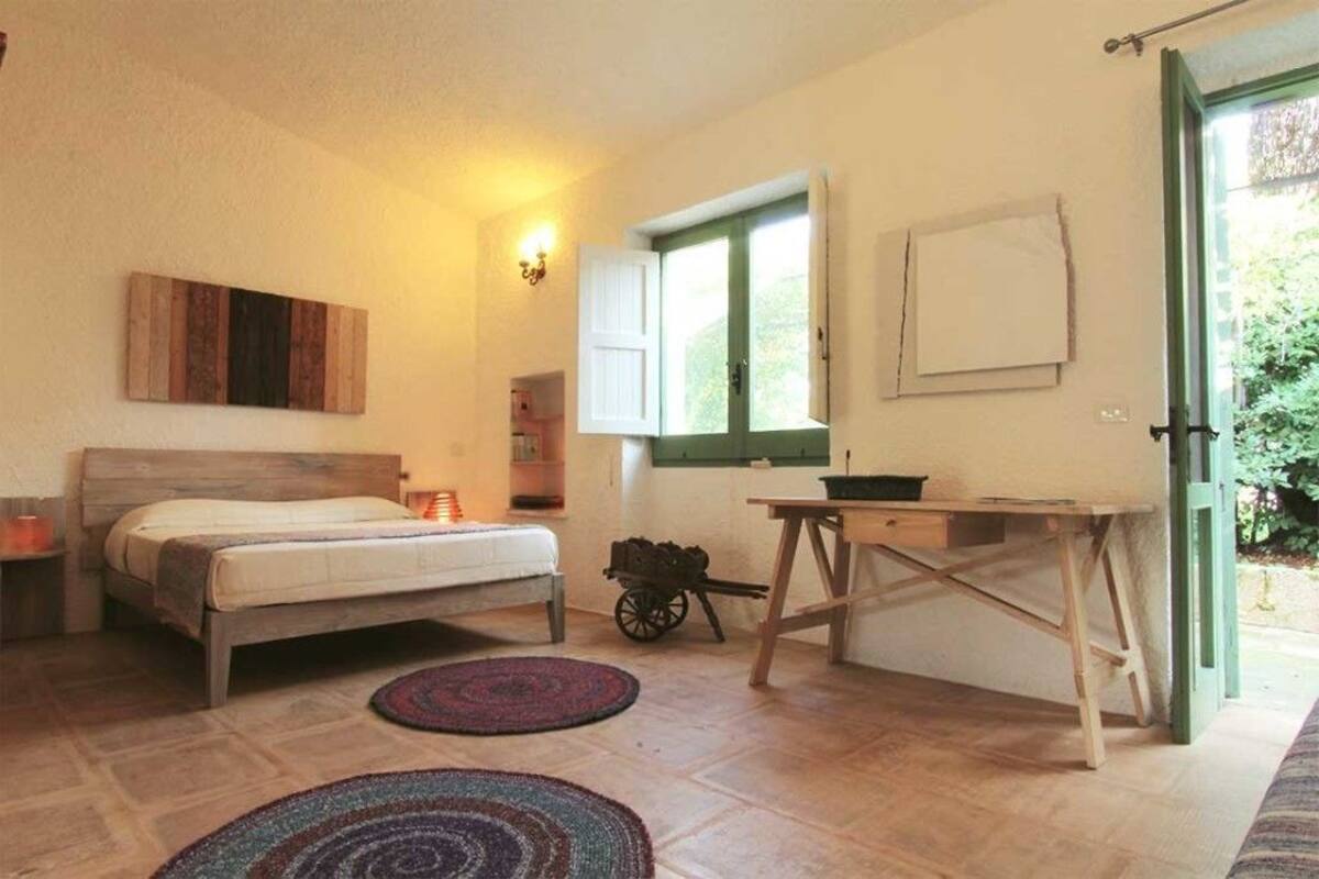 Une chambre à coucher avec un lit, une petite table, une chaise, une fenêtre et une porte.