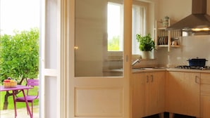 A kitchen with wooden cabinets, a stove, and a window overlooking a garden. - Masseria Gianferrante (Ugento)