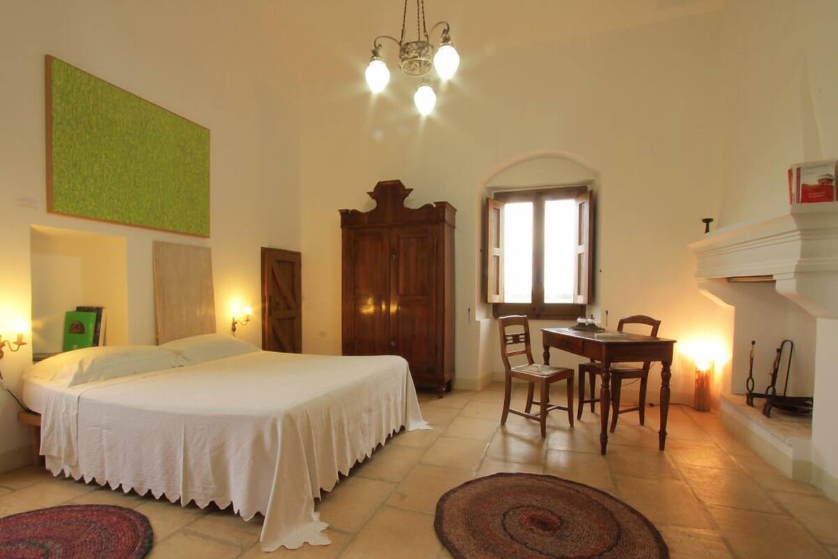 Une chambre à coucher avec un lit, un bureau, une chaise, une cheminée et une fenêtre.