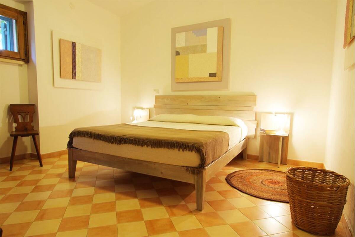 Une chambre à coucher avec un lit en bois, deux lampes fixées au mur, un panier en osier et un sol à carreaux.