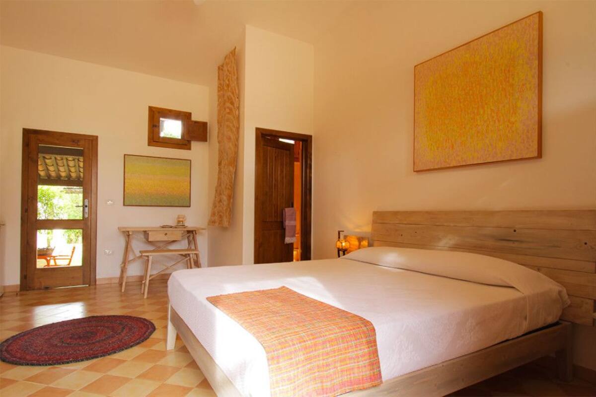 Une chambre avec un lit en bois, un bureau et une chaise. Une porte donne accès à un espace extérieur.