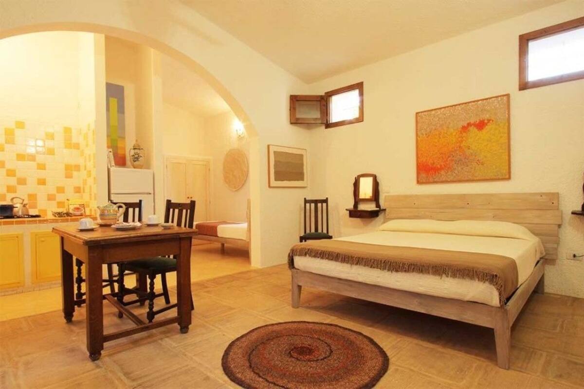 Une chambre avec un lit en bois, une table à manger avec des chaises, un coin cuisine et une petite salle de bain.