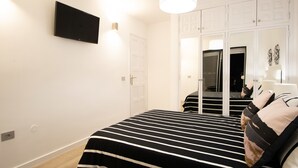 Ein Schlafzimmer mit einem Bett, einem an der Wand montierten Fernseher, einem Kleiderschrank und einem Spiegel.