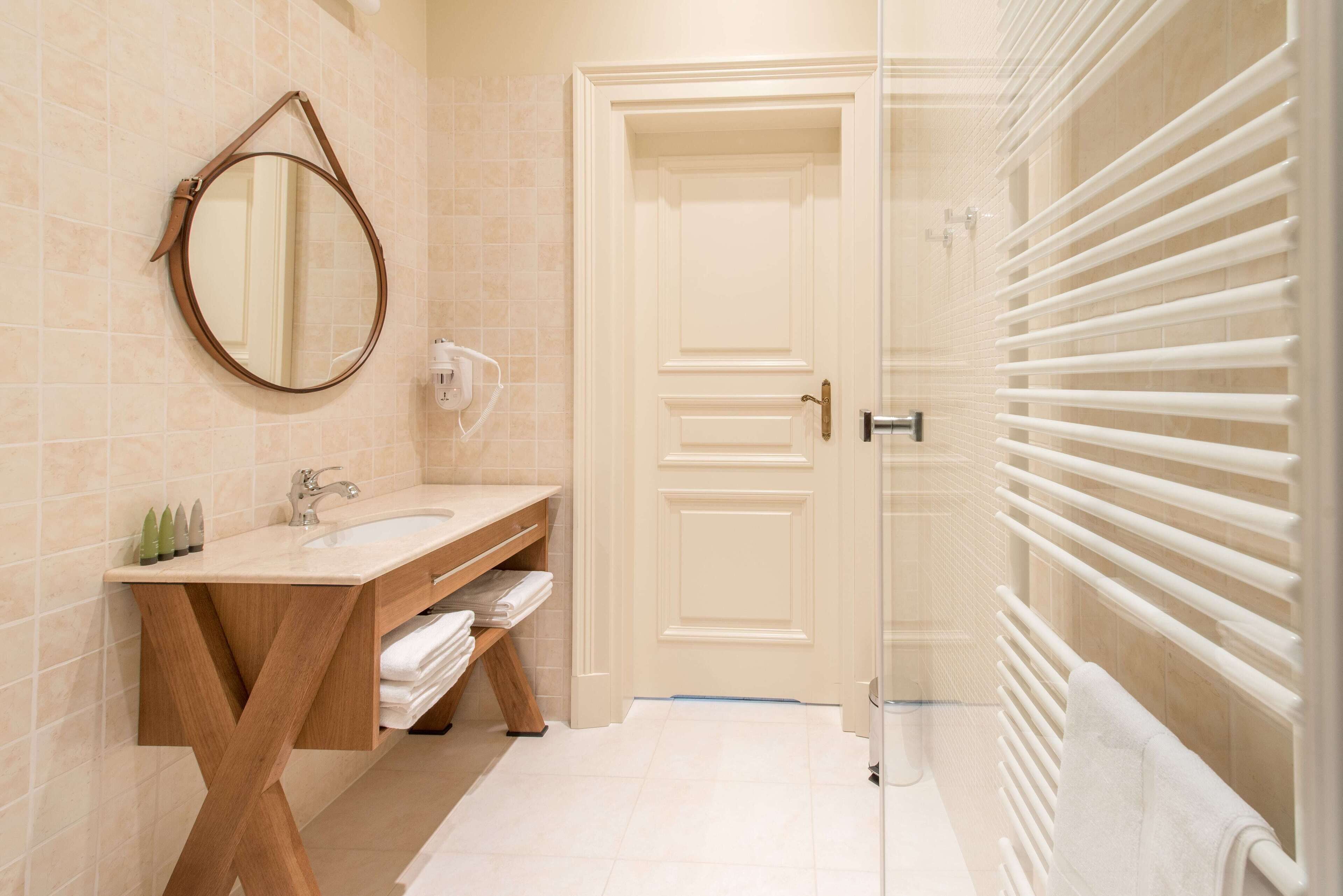 A bathroom with a wooden vanity, a round mirror, a white door, and a white towel rack.