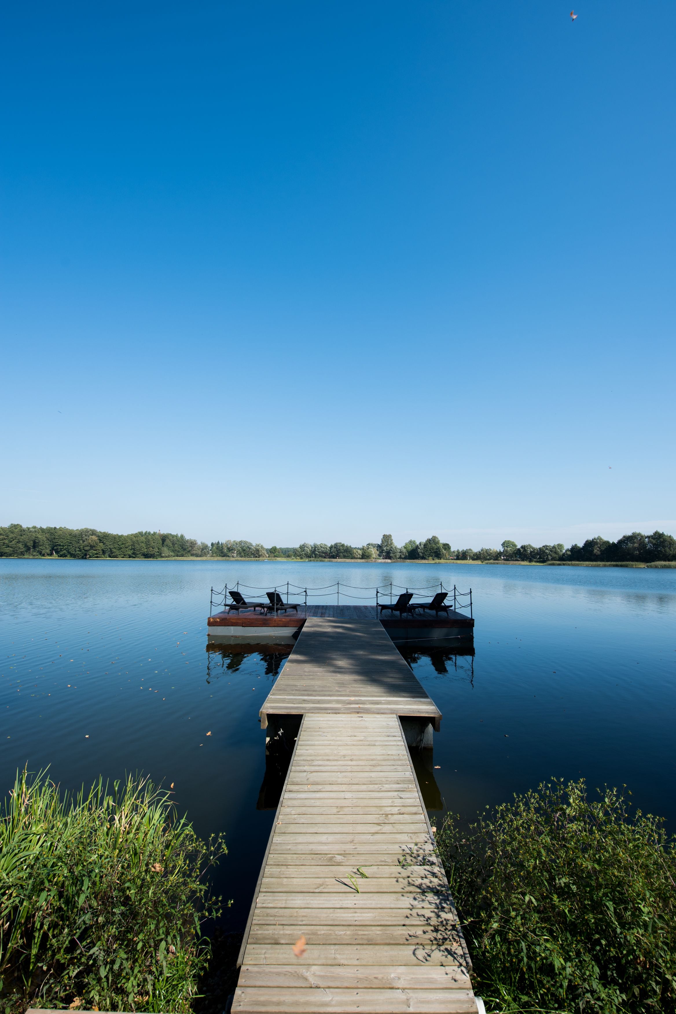 A wooden dock extending into calm water with two boats moored at the end.