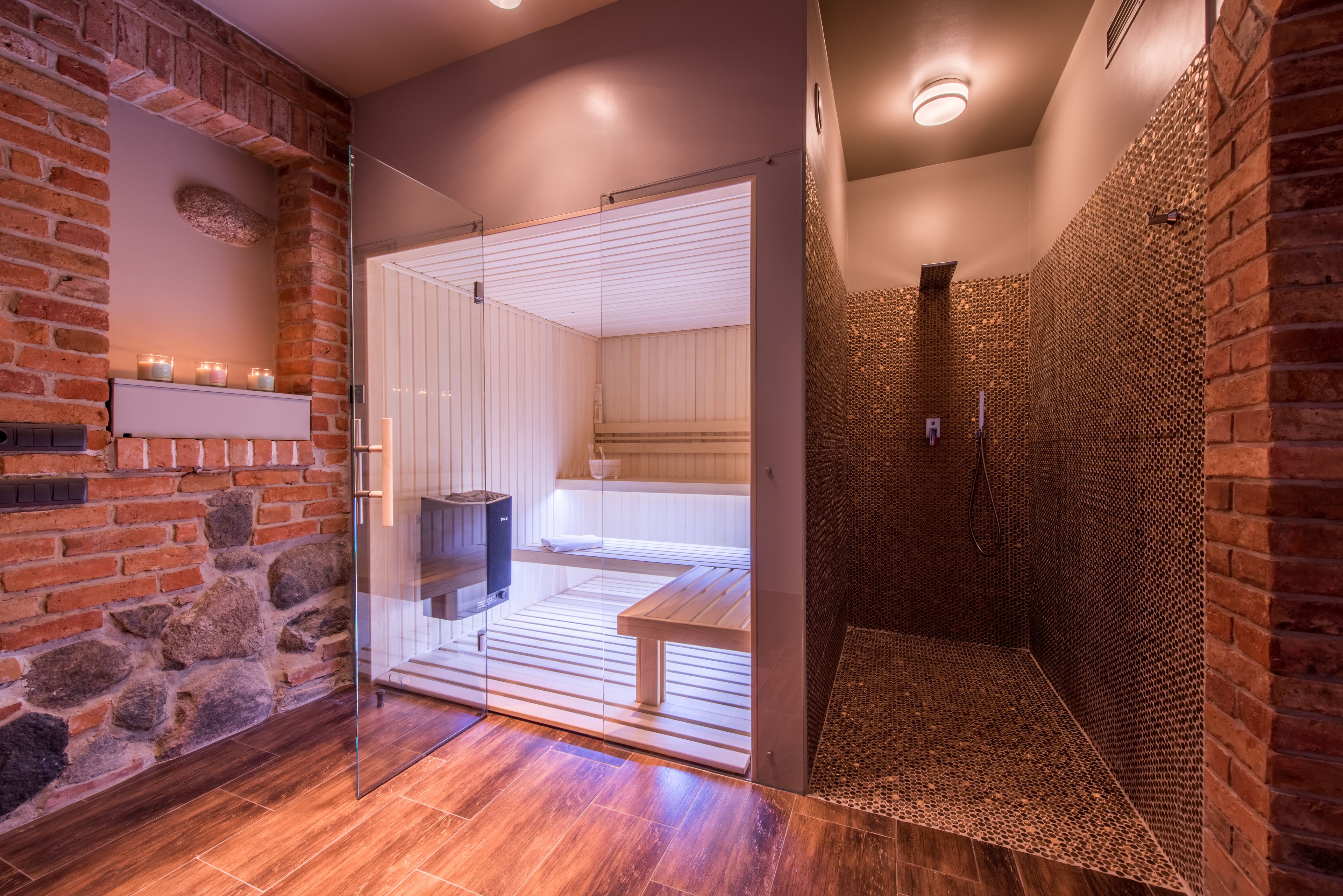 A modern bathroom with a glass shower enclosure, a wooden bench, and a stone wall.