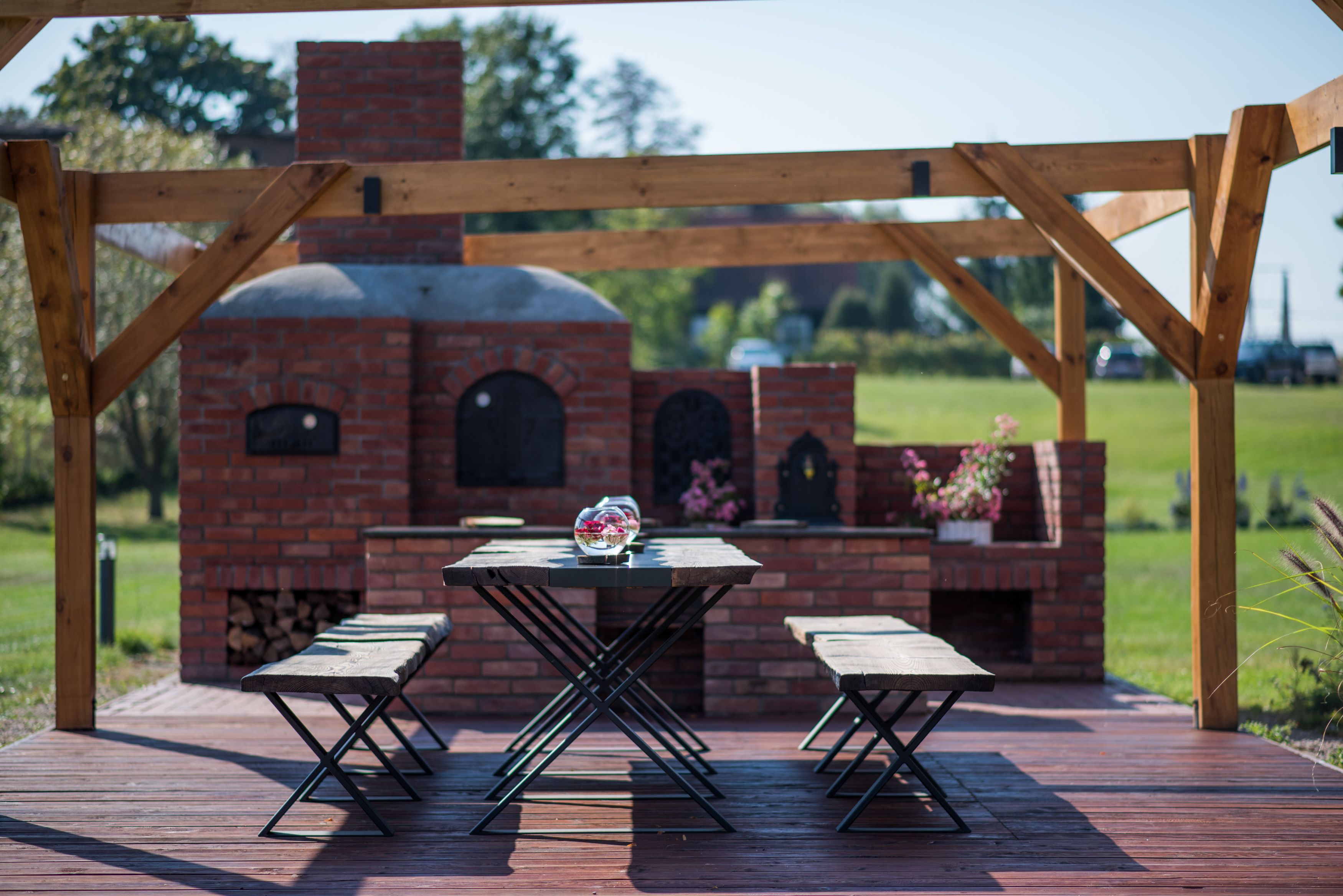 A brick outdoor kitchen with a wooden pergola, a table, and two benches.