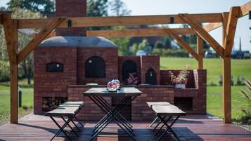 A brick outdoor kitchen with a wooden pergola, a table, and two benches.