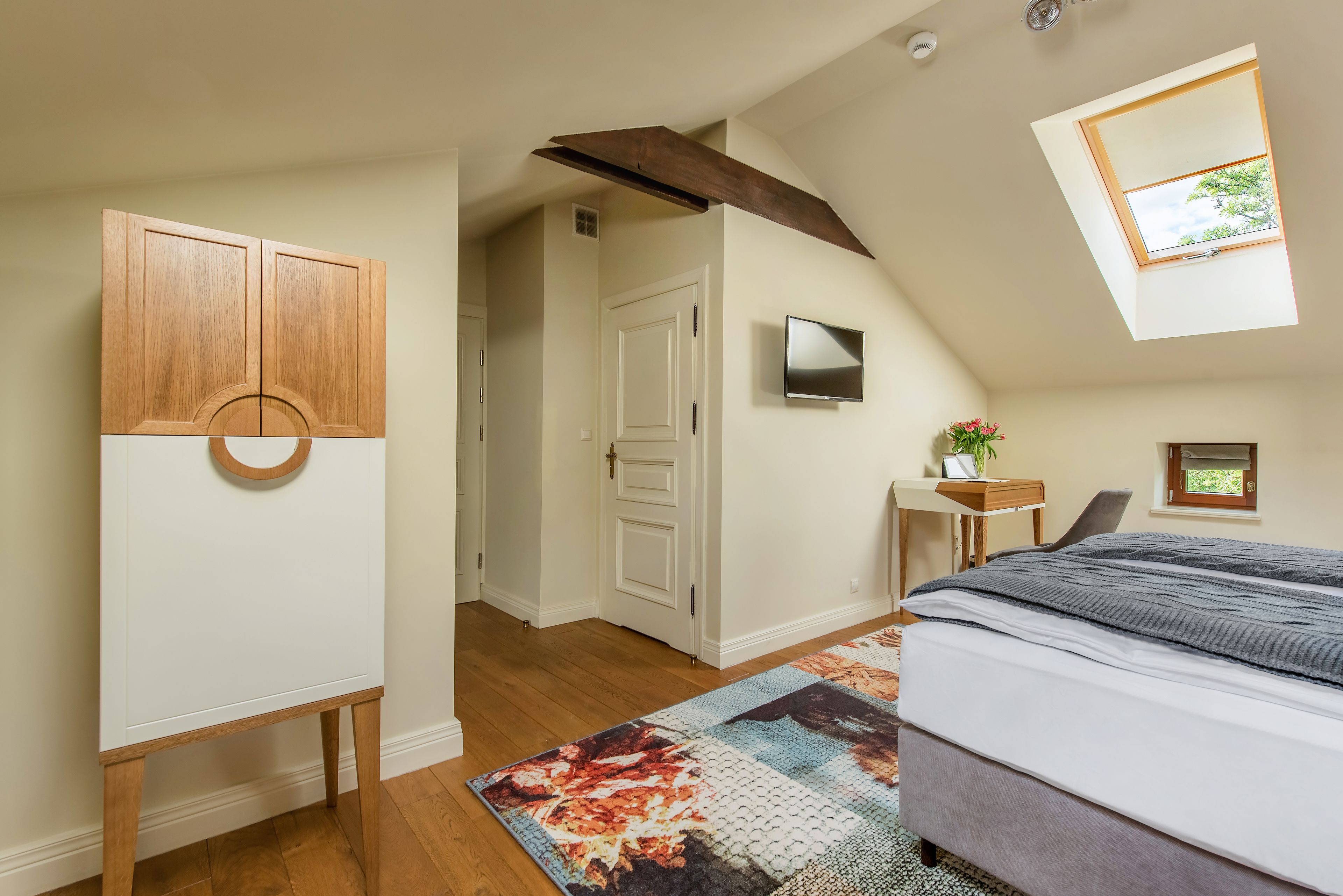 A bedroom with a sloped ceiling, a large bed, a TV on the wall, and a window.