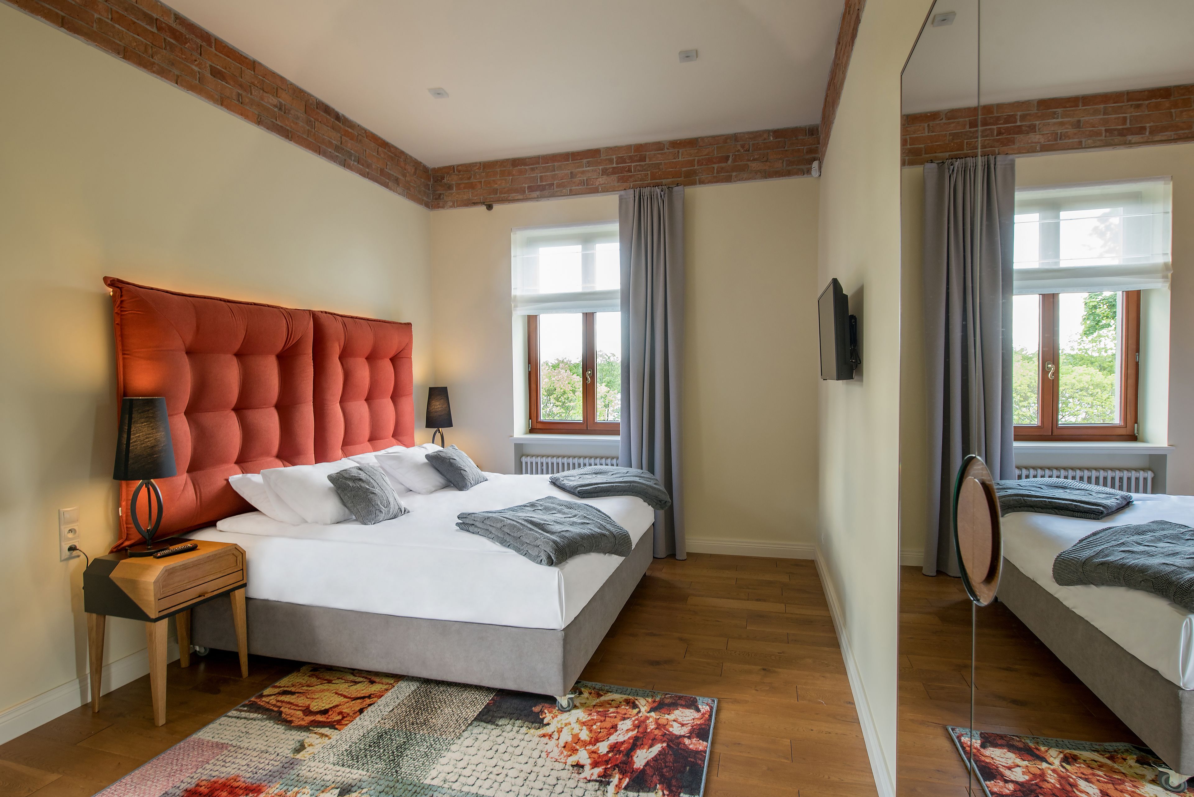 A bedroom with a large bed, a nightstand, a mirror, and a window with curtains.